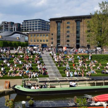 London, UK - May 12 2024: People enjoy the sunshine on the steps covered with green artificial turf at Granary Square next to Central Saint Martins and Regent's Canal in King's Cross.